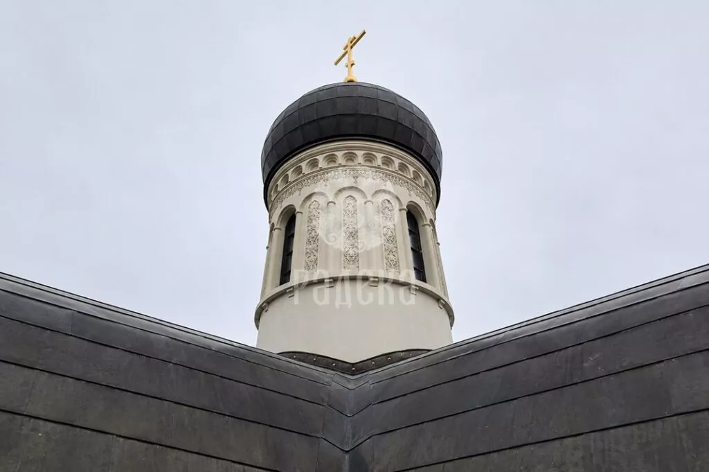 Dark dome with a golden cross above the carved drum and metal roof of the church.