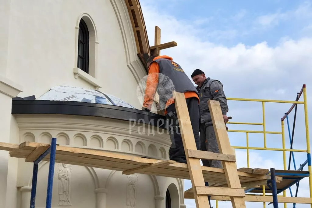 RADEKA craftsmen install the metal covering of the church's rounded roof from scaffolding.