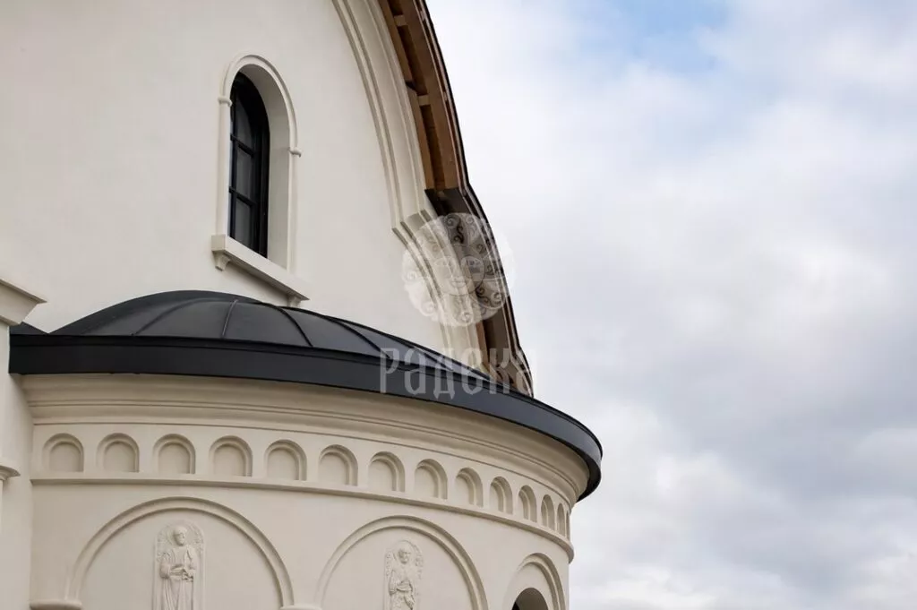 Rounded metal roof above the relief facade of the church with an arched window.