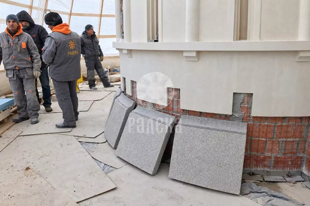 Craftsmen at the rounded facade of the church and prepared stone elements for the plinth cladding.