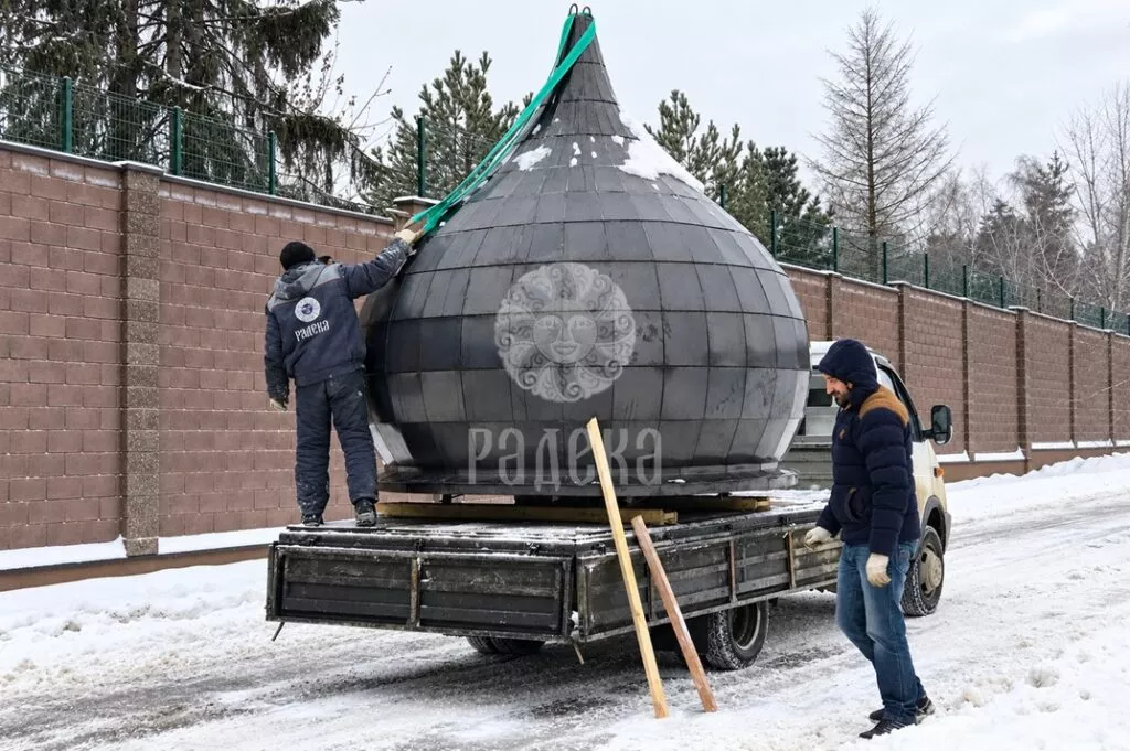 Workers prepare the metal dome on the truck for unloading using green straps.