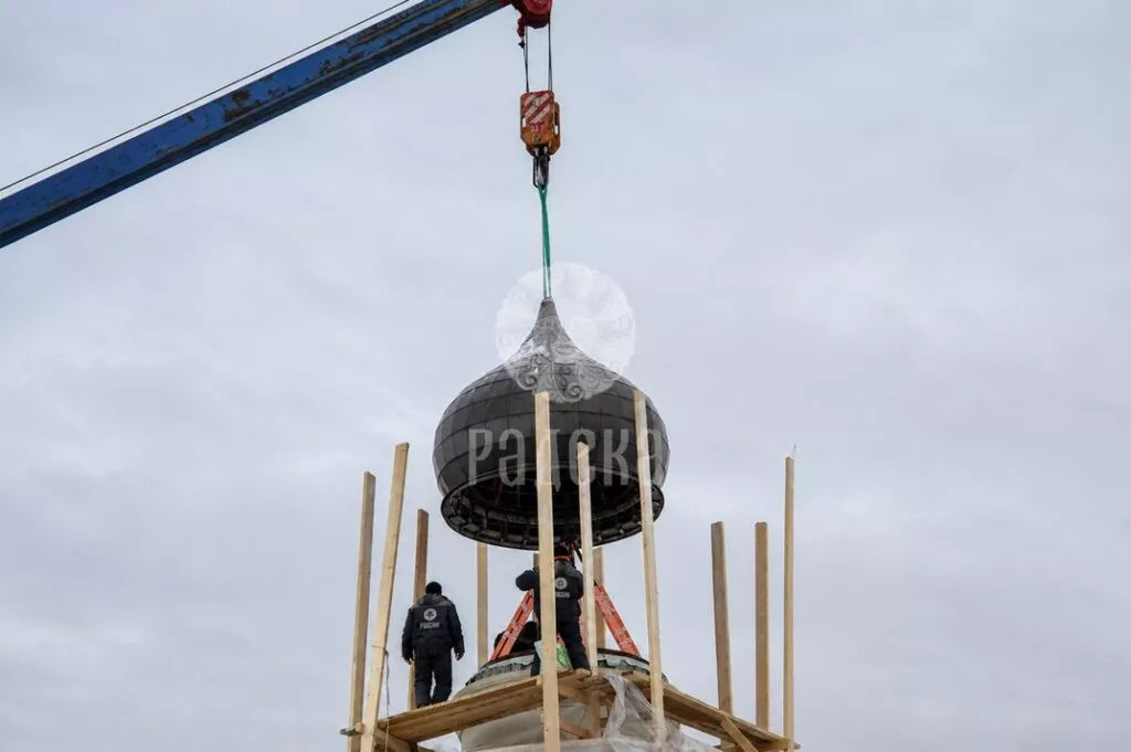 Installers receive the dome lowered by a crane above the upper part of the church.