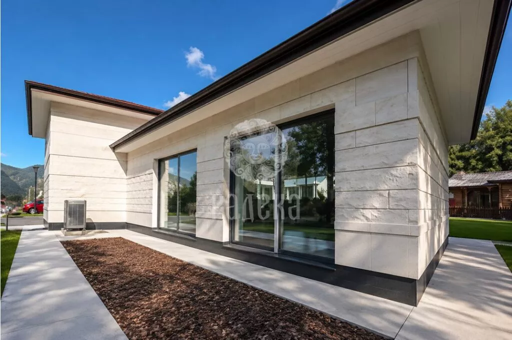 Facade of the house in Barvikha with light stone cladding and panoramic windows.
