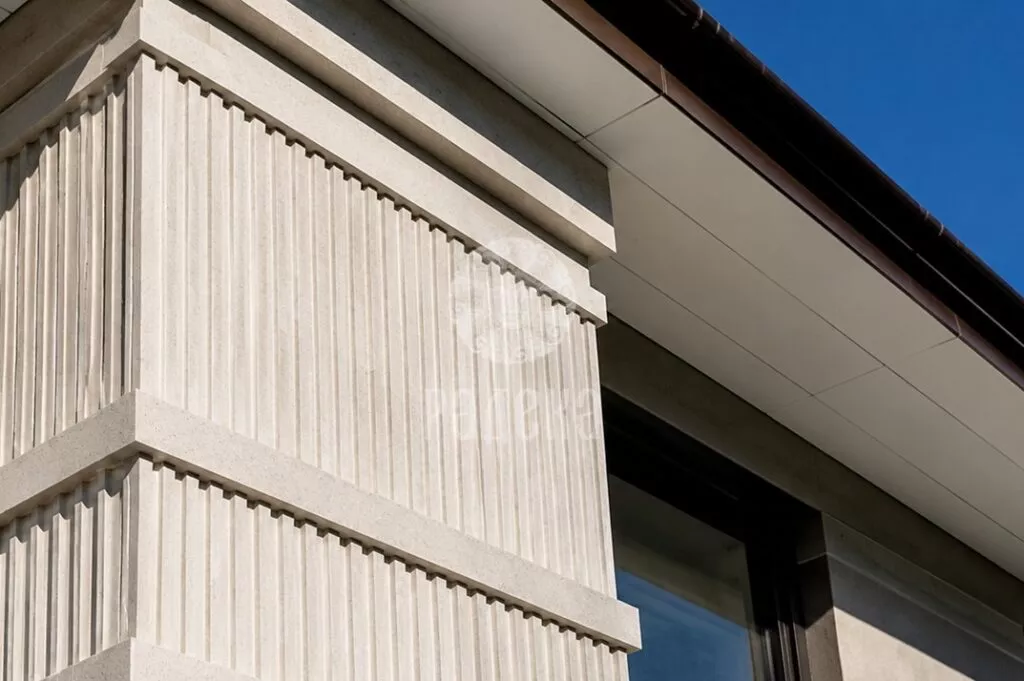Stone corner element with vertical flutes and horizontal bands under the roof overhang.