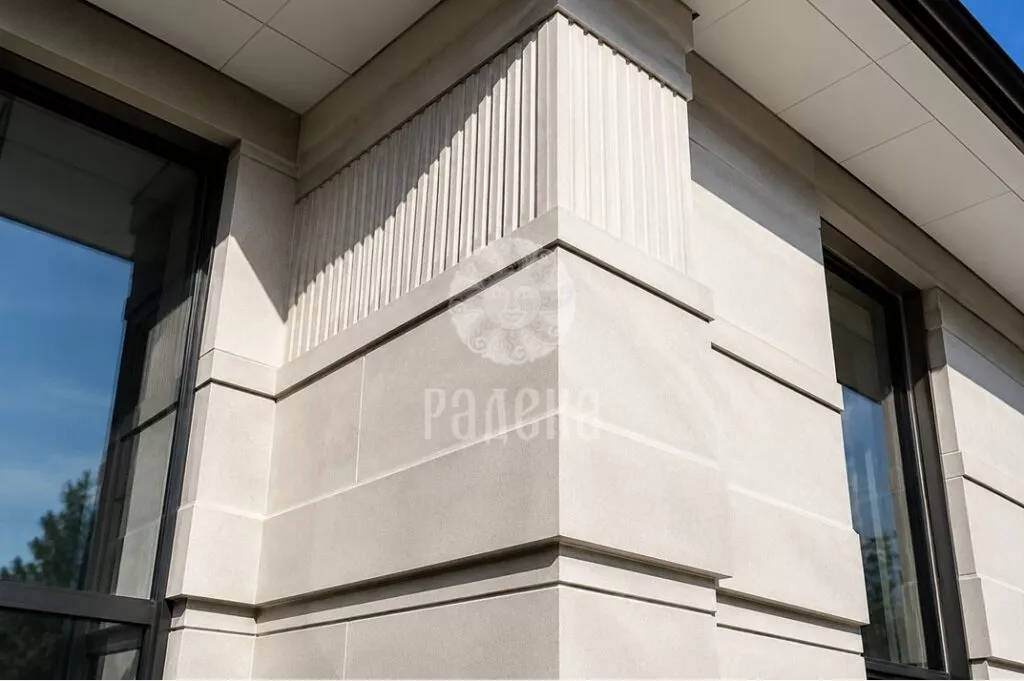 Corner of the facade with vertical flutes at the top and smooth stone slabs at the bottom.