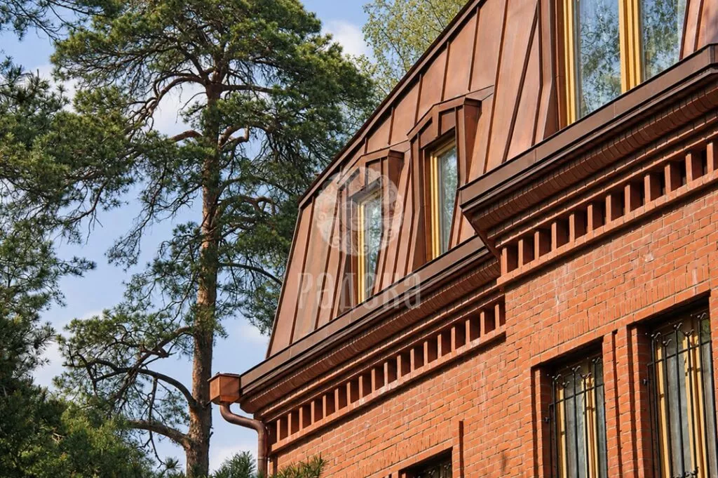 Copper mansard roof above a brick facade among pine trees