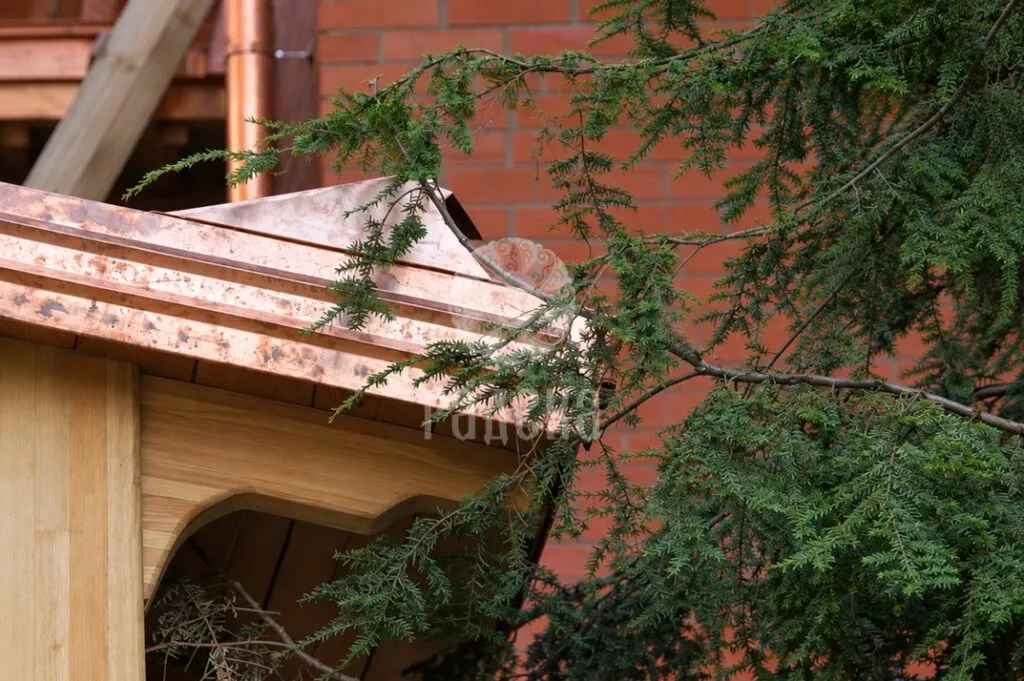 Copper finishing of the edge of a wooden canopy behind pine branches