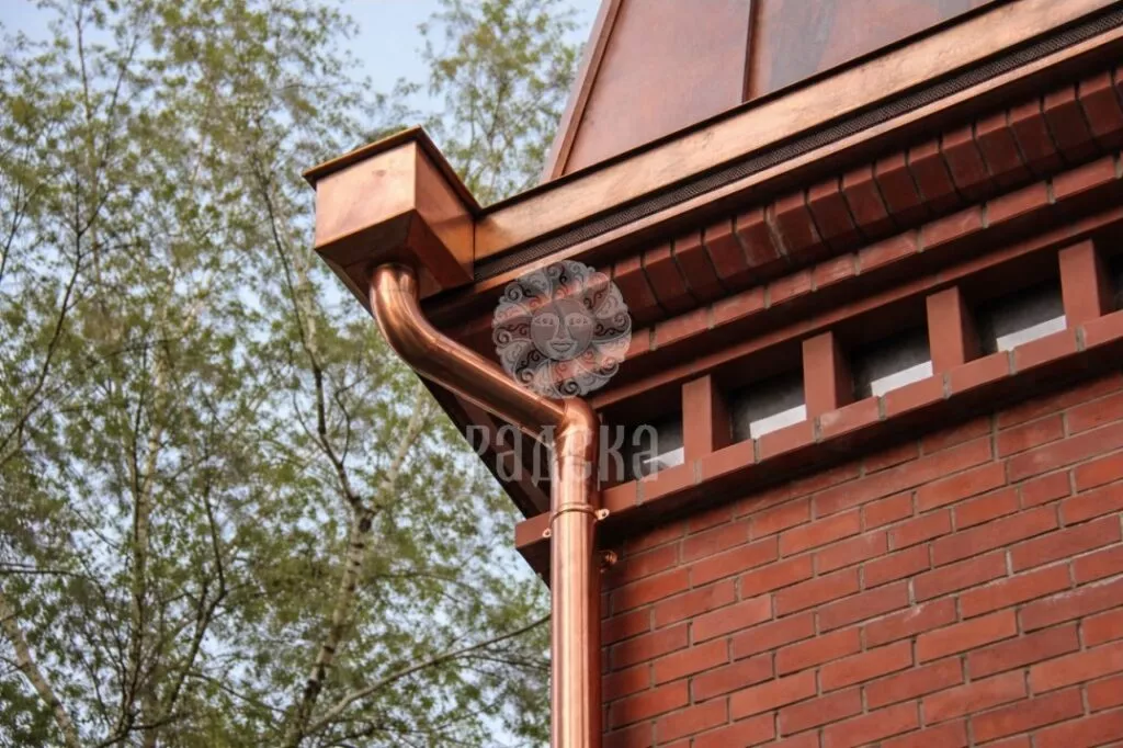Copper hopper head and offset downpipe beside the brick cornice