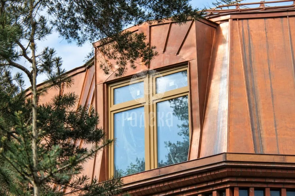 Large dormer window with copper cladding behind pine branches