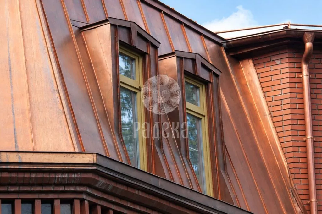Two narrow dormer windows in the copper roof next to the brick part of the house