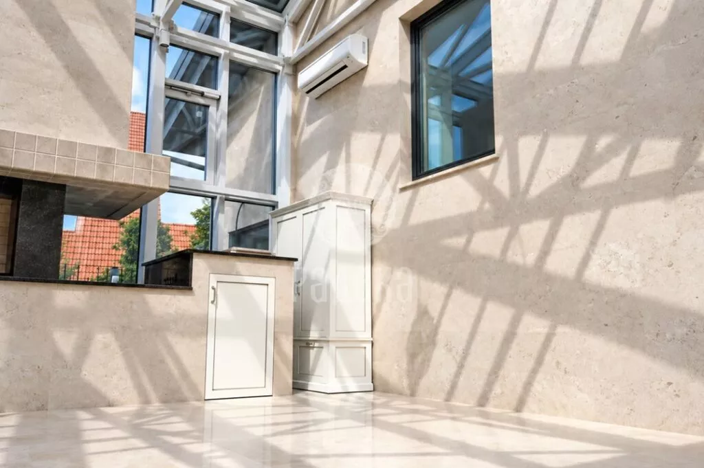Stone wall, light built-in cabinets, and part of the barbecue with a dark countertop in a sunny room