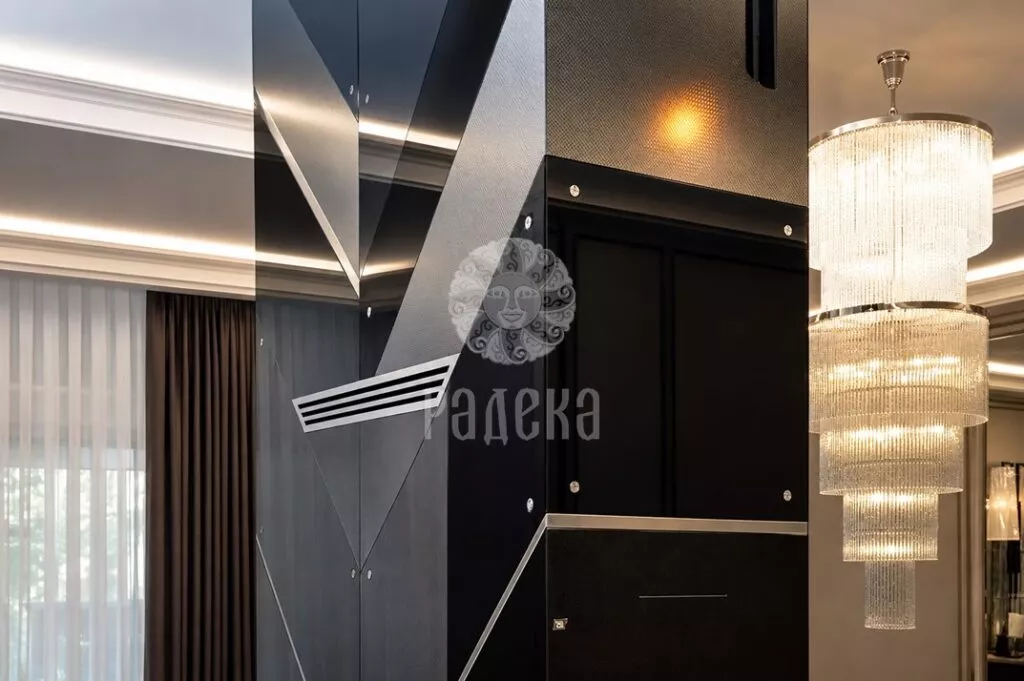 Side view of the fireplace with textured and reflective panels, diagonal joints, and a chandelier in the background.