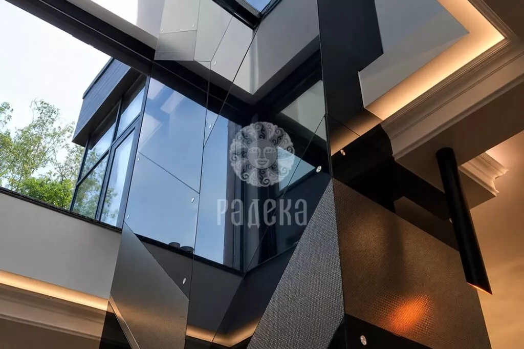 Upper section of the fireplace beside the windows in a double-height space, with reflective surfaces and geometric cladding joints.