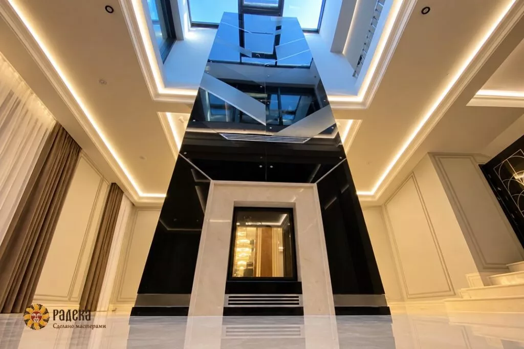 Seven-meter-tall, double-sided fireplace at Rublyovo Residence, with a Crema Marfil marble surround and dark geometric cladding beneath a skylight.