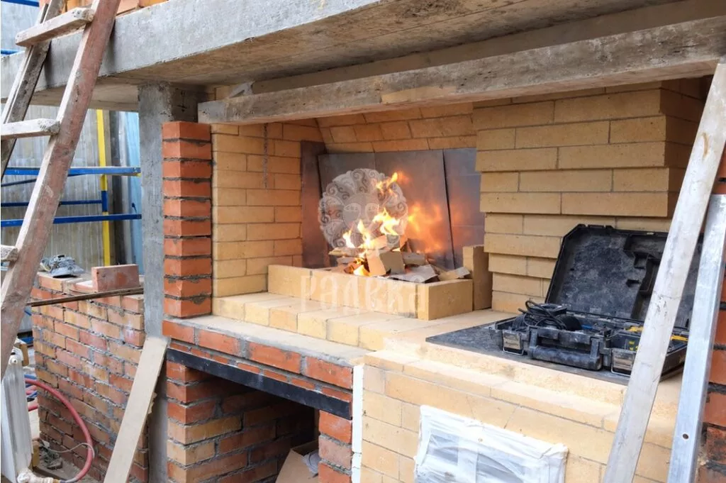 Fire burning in the brick barbecue firebox before natural stone cladding is installed.