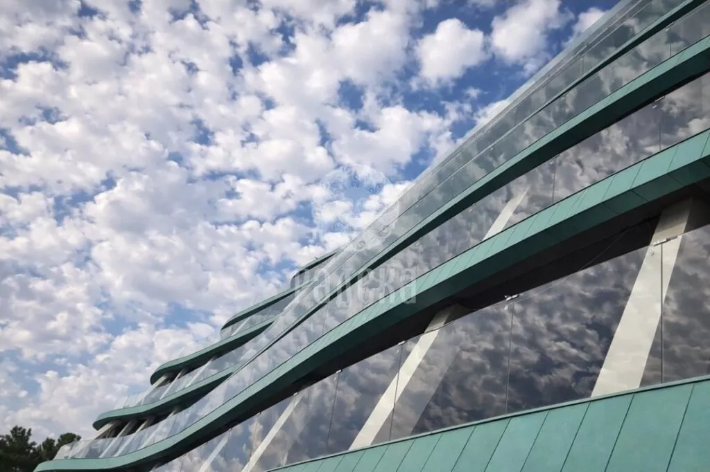 Clouds reflected in the glass railings of the Reef Residence balconies between green copper belts.