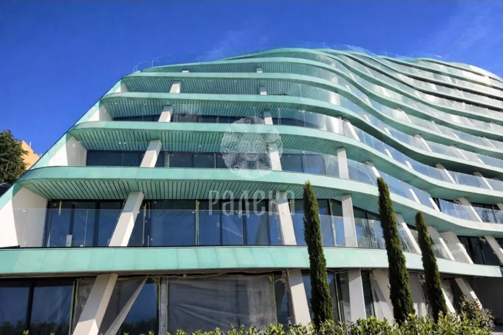 Curved balconies of Reef Residence with green copper cladding and soffits against the blue sky.